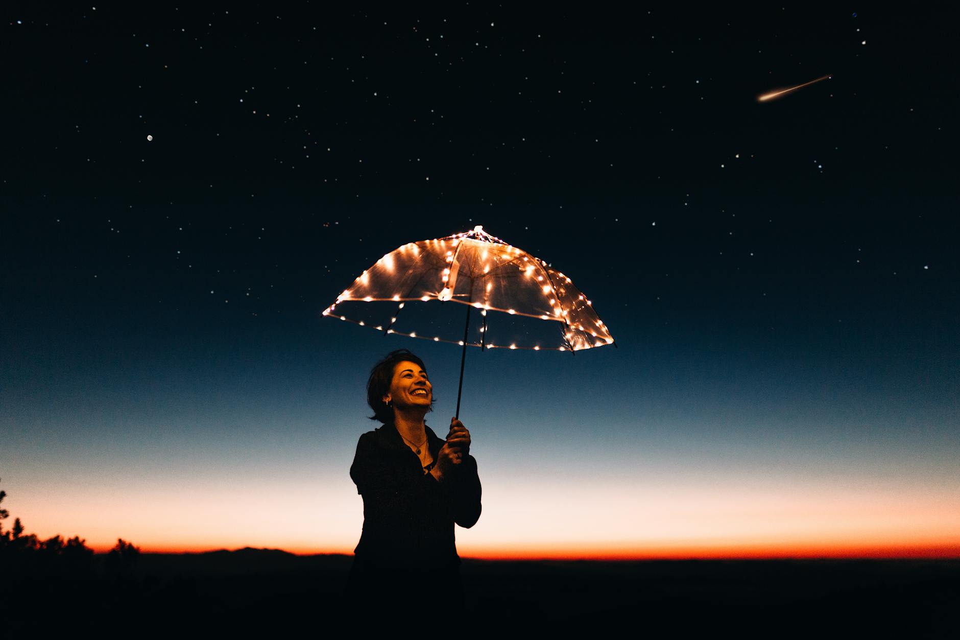 A joyful woman with a light-up umbrella stands under a starry sky, capturing a magical moment. A joyful woman with a light-up umbrella stands under a starry sky, capturing a magical moment.