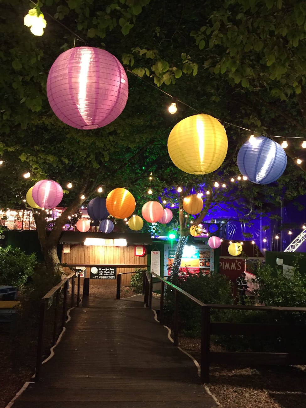 Vibrant paper lanterns hanging over a garden path during a festive night celebration outdoors. Vibrant paper lanterns hanging over a garden path during a festive night celebration outdoors.