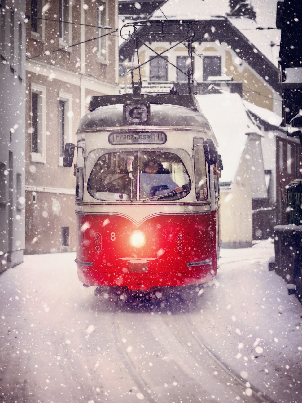 A red tram moving through snow-covered streets in Gmunden, Austria, during winter snowfall.