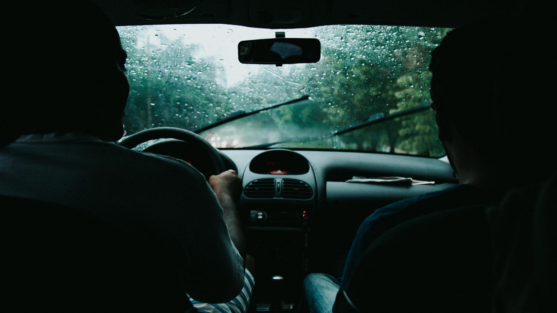 Two people drive through rainy São Paulo streets, wet windshield and raindrops visible.
