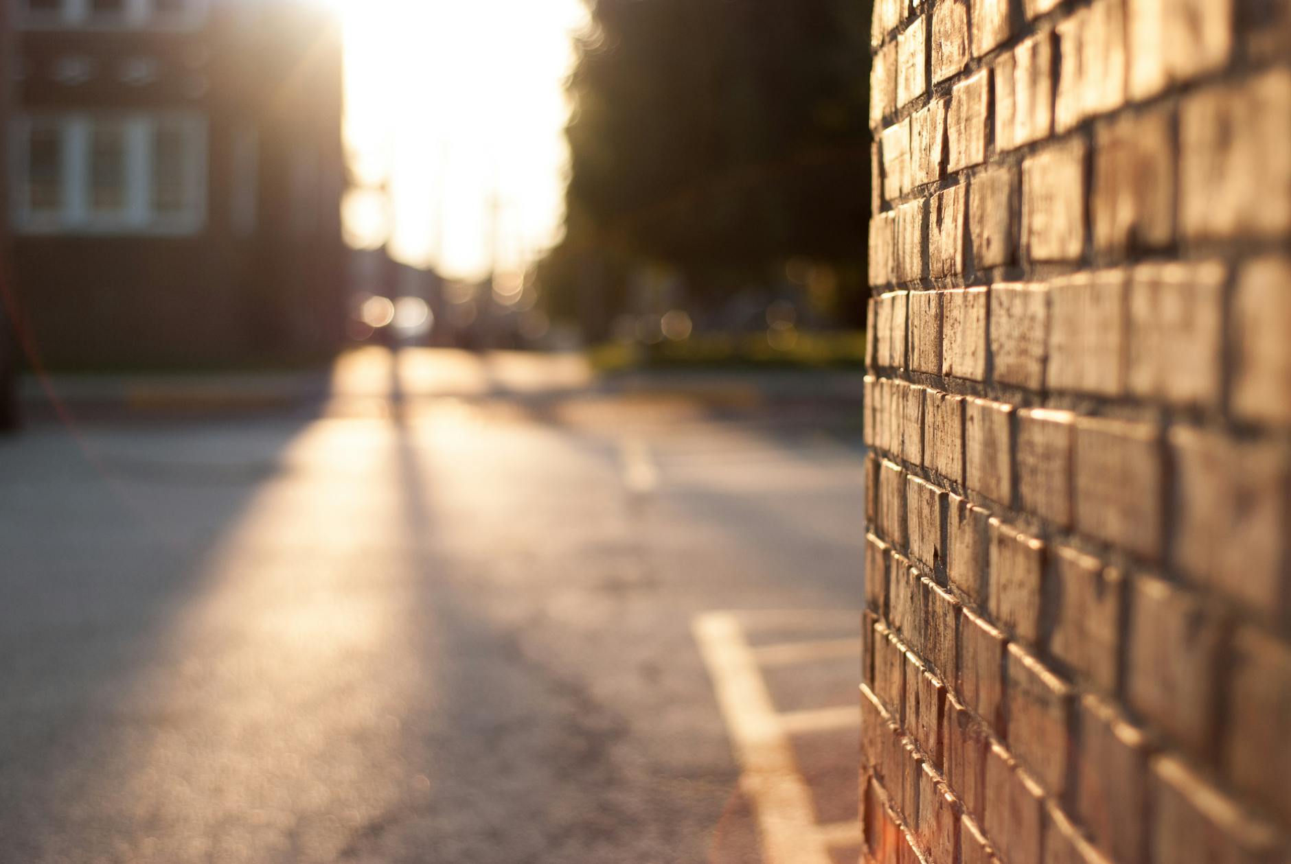 Close-up of a sunlit brick wall with blurred urban street in the background at sunset. Close-up of a sunlit brick wall with blurred urban street in the background at sunset.
