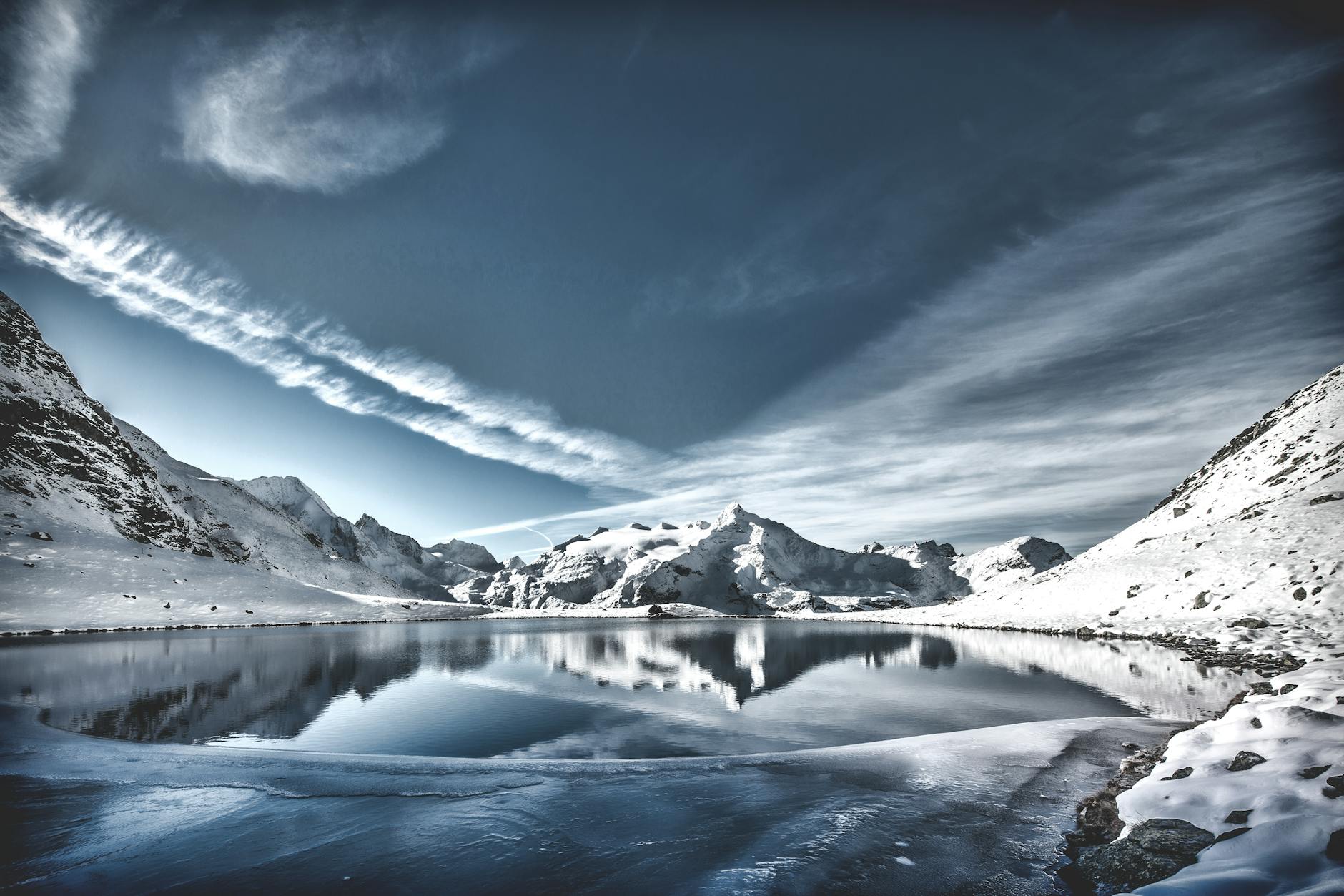 A breathtaking view of a snowy mountain lake reflecting the sky, with serene winter scenery.
