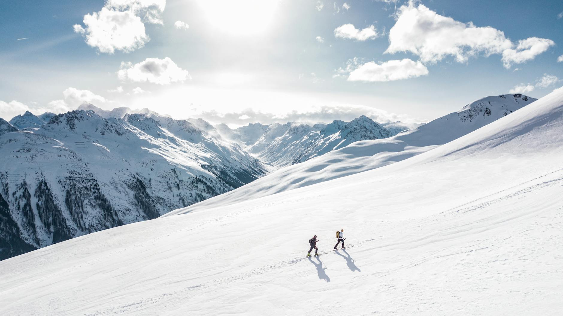 Two skiers climbing a sunlit snowy mountain slope in Ischgl, Austria, during winter. Two skiers climbing a sunlit snowy mountain slope in Ischgl, Austria, during winter.