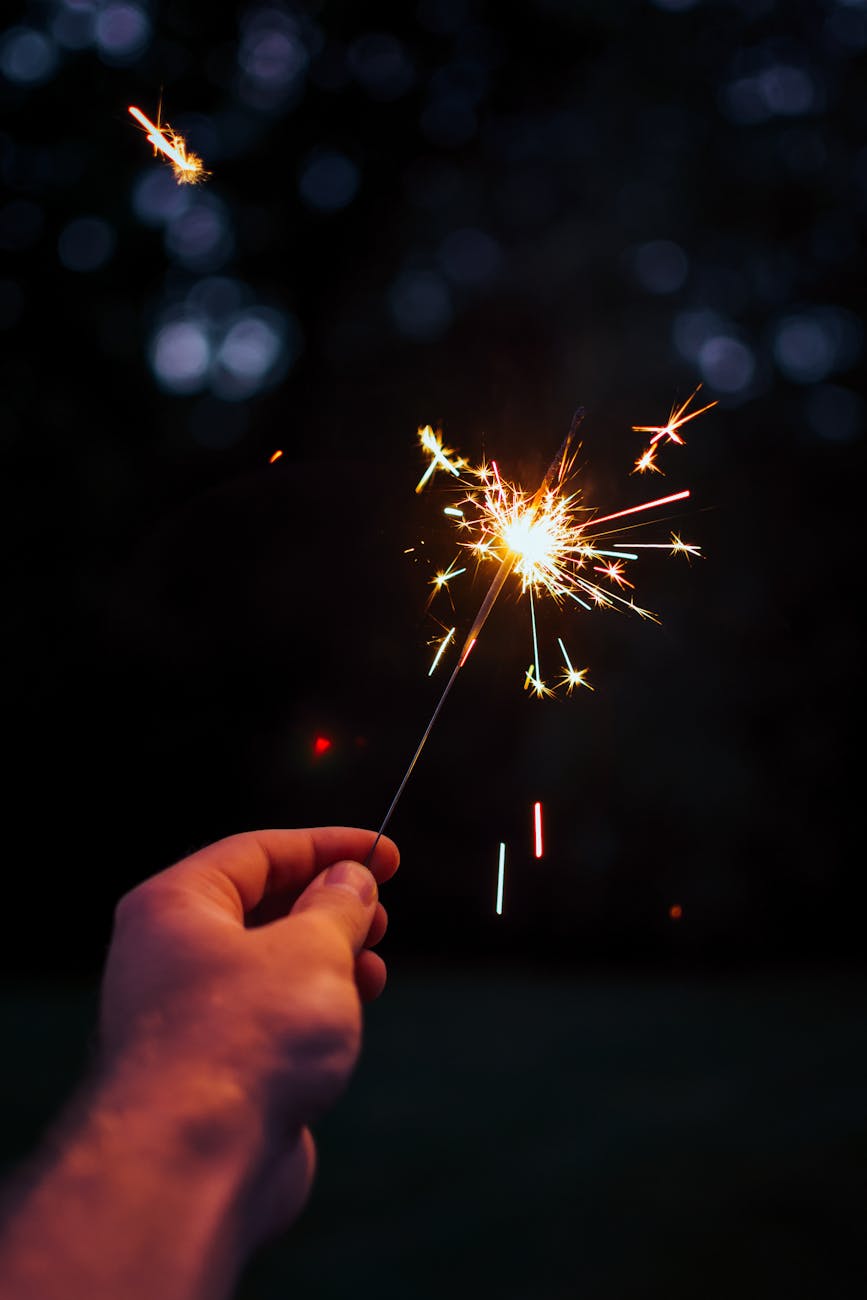 A person holding a bright sparkler outdoors in a festive night setting. A person holding a bright sparkler outdoors in a festive night setting.
