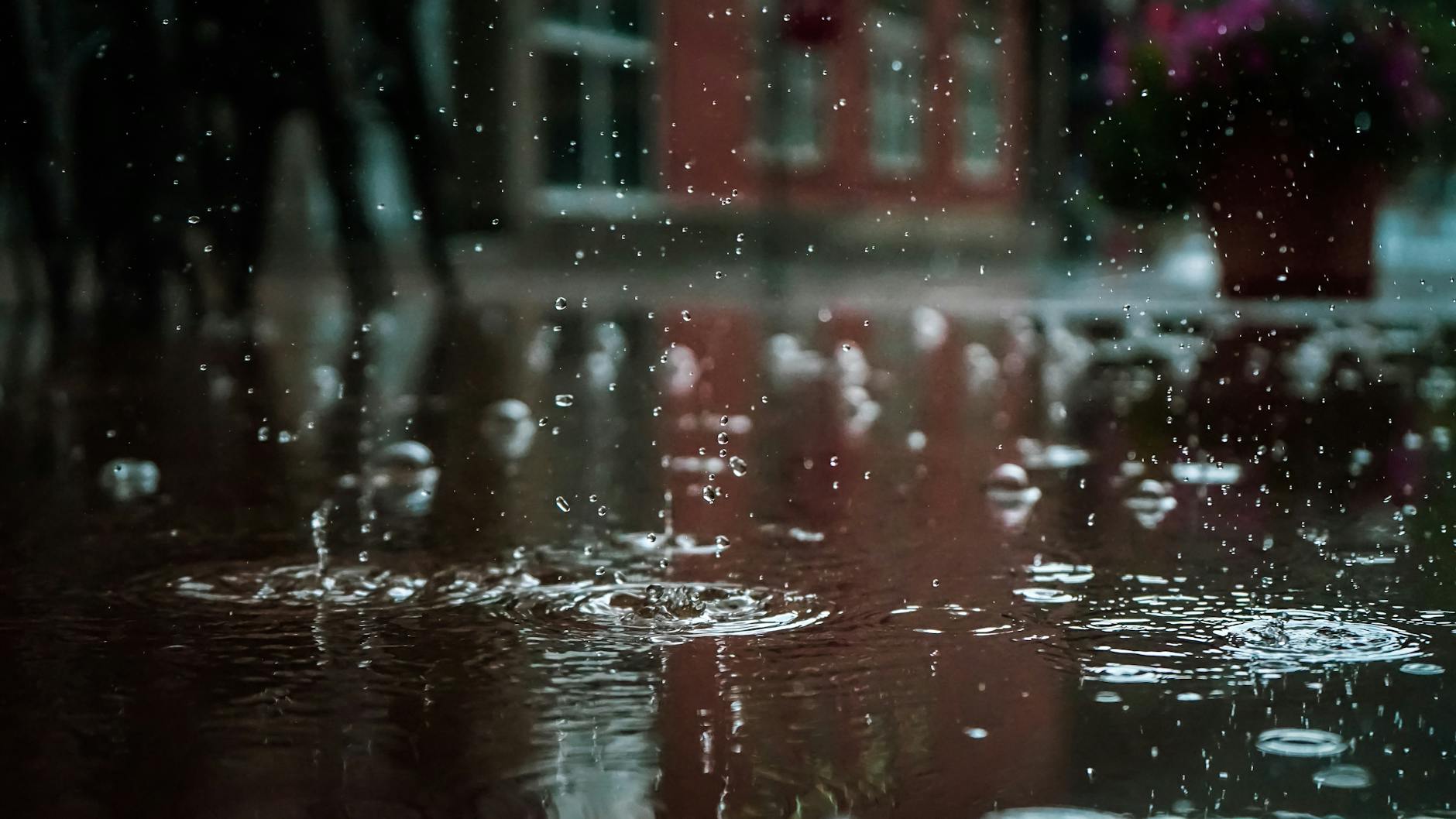 Close-up of raindrops splashing into a puddle, capturing reflections and textures in an outdoor urban setting. Close-up of raindrops splashing into a puddle, capturing reflections and textures in an outdoor urban setting.