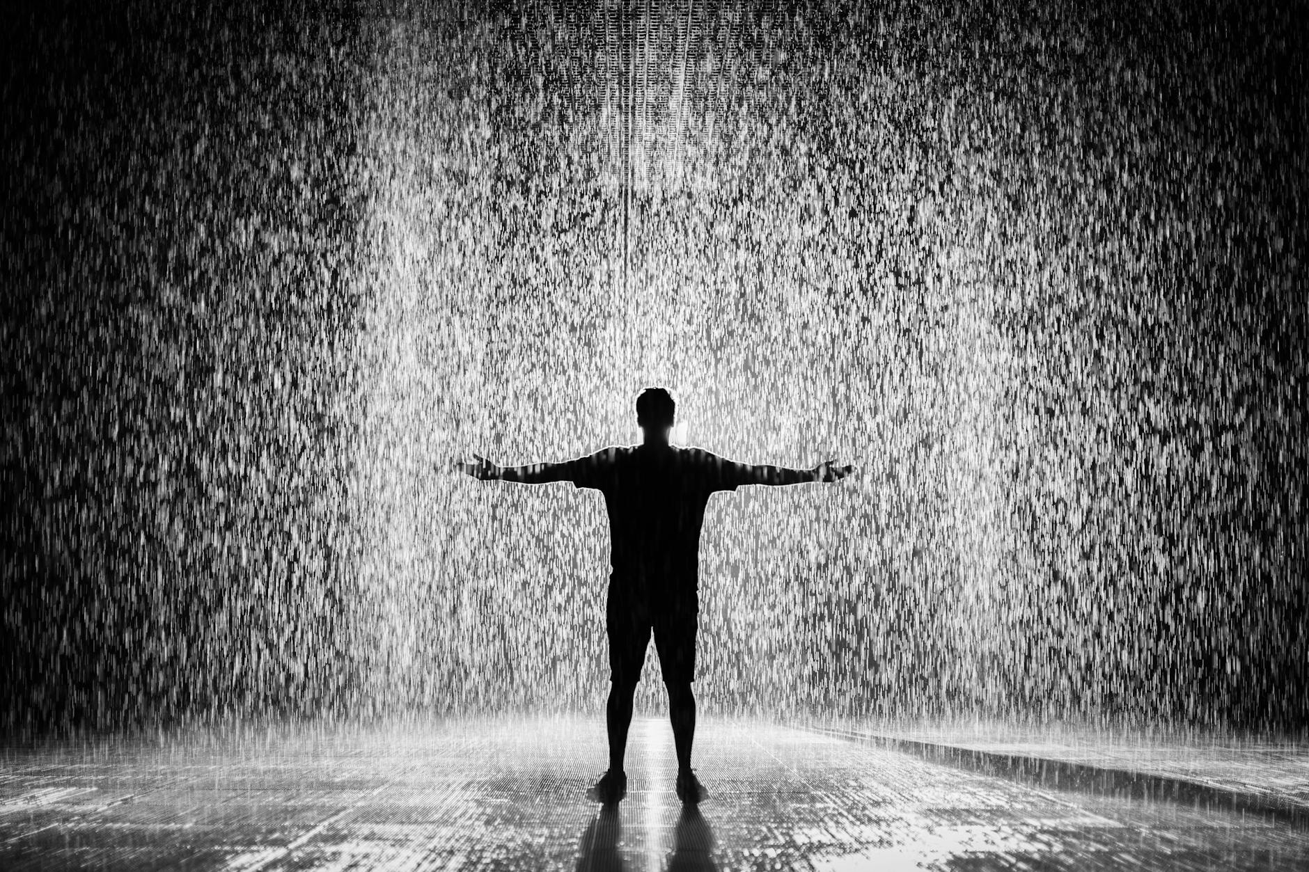 A person joyfully standing in the rain with arms wide open in a dramatic black and white scene. A person joyfully standing in the rain with arms wide open in a dramatic black and white scene.