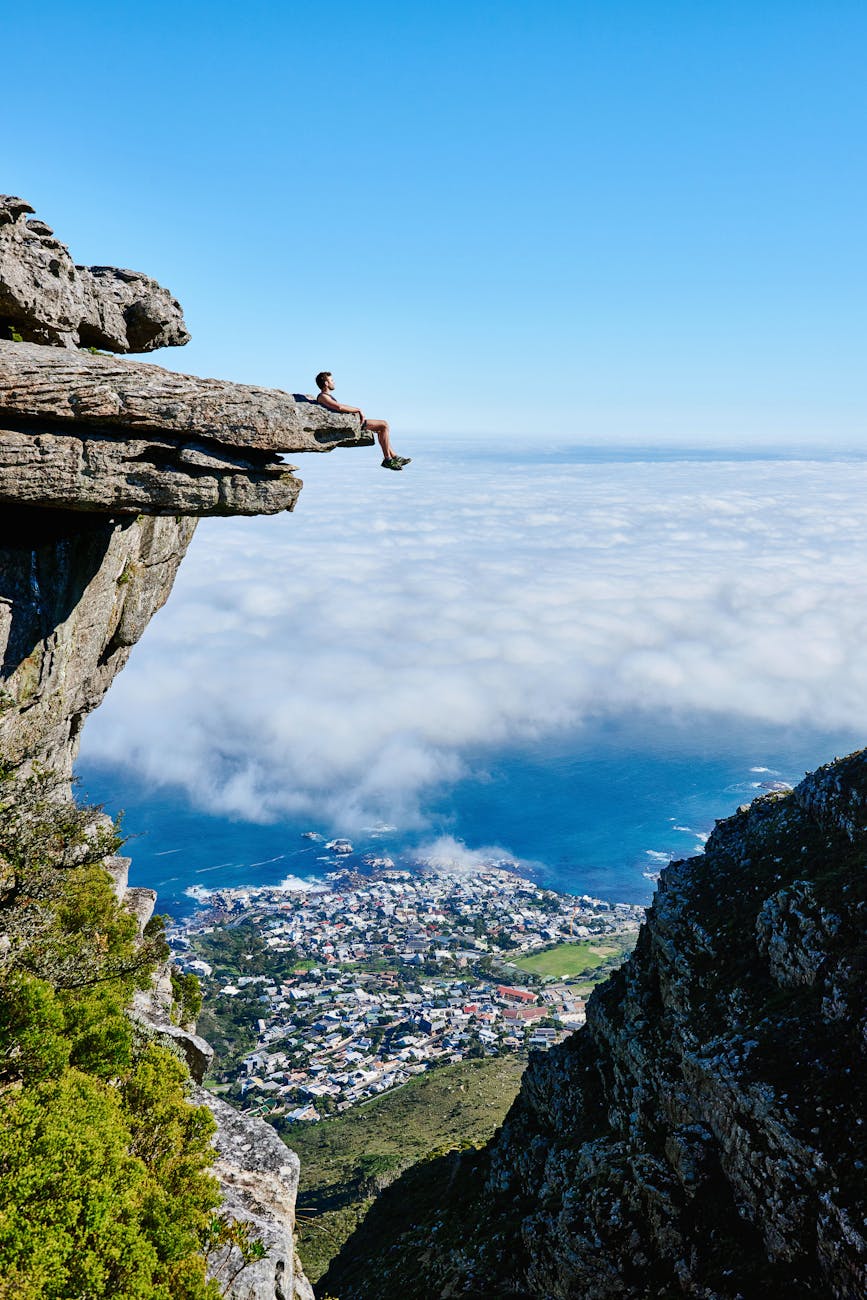 A person sits on a cliff edge enjoying a breathtaking view of the ocean and city below. A person sits on a cliff edge enjoying a breathtaking view of the ocean and city below.