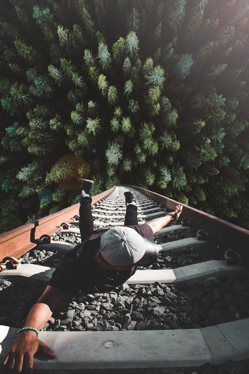 A man poses daringly over train tracks with a forest view. A man poses daringly over train tracks with a forest view.