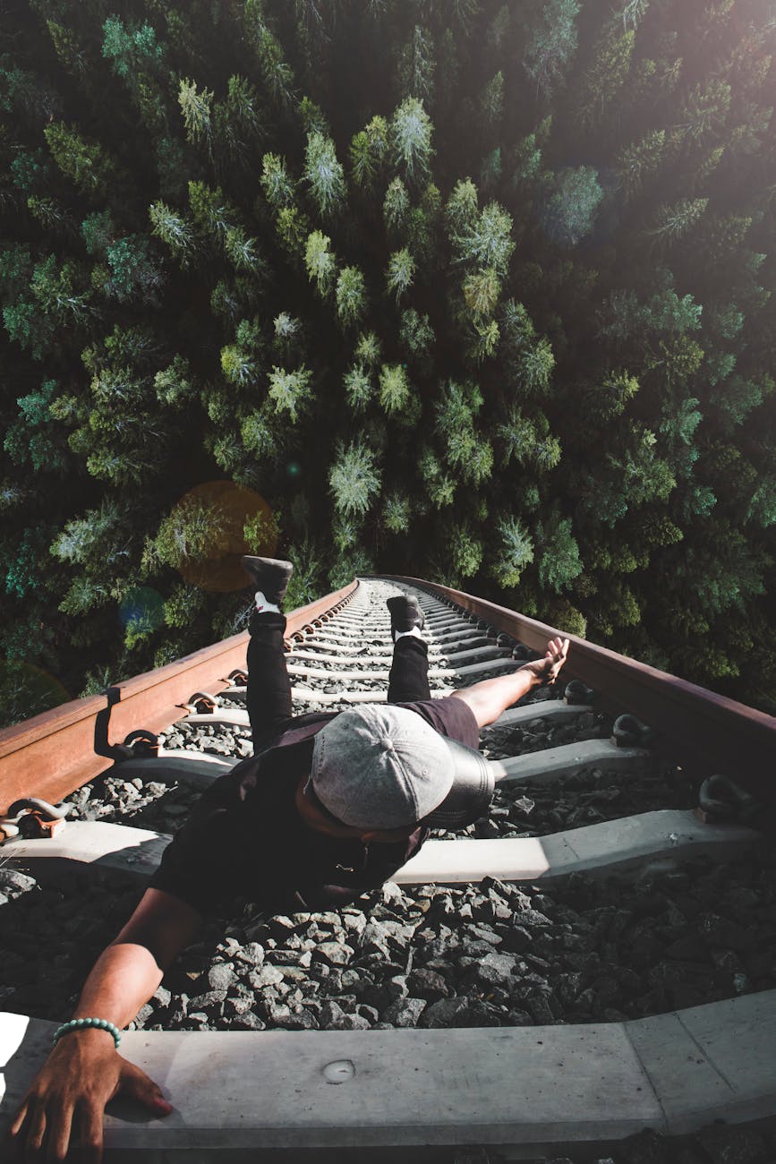 A man poses daringly over train tracks with a forest view. A man poses daringly over train tracks with a forest view.