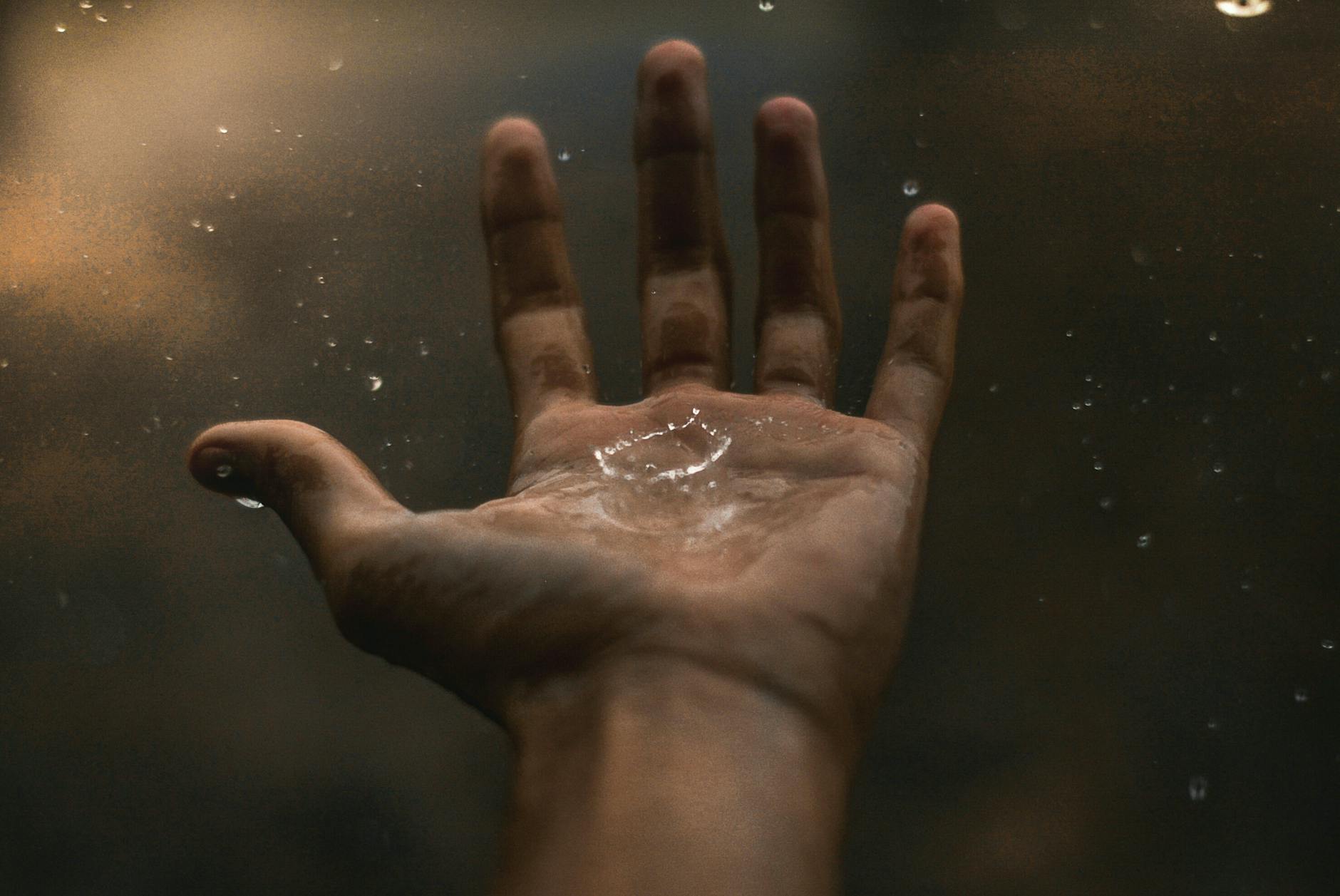 A close-up of an open hand catching raindrops against a dark background, showcasing water interaction. A close-up of an open hand catching raindrops against a dark background, showcasing water interaction.