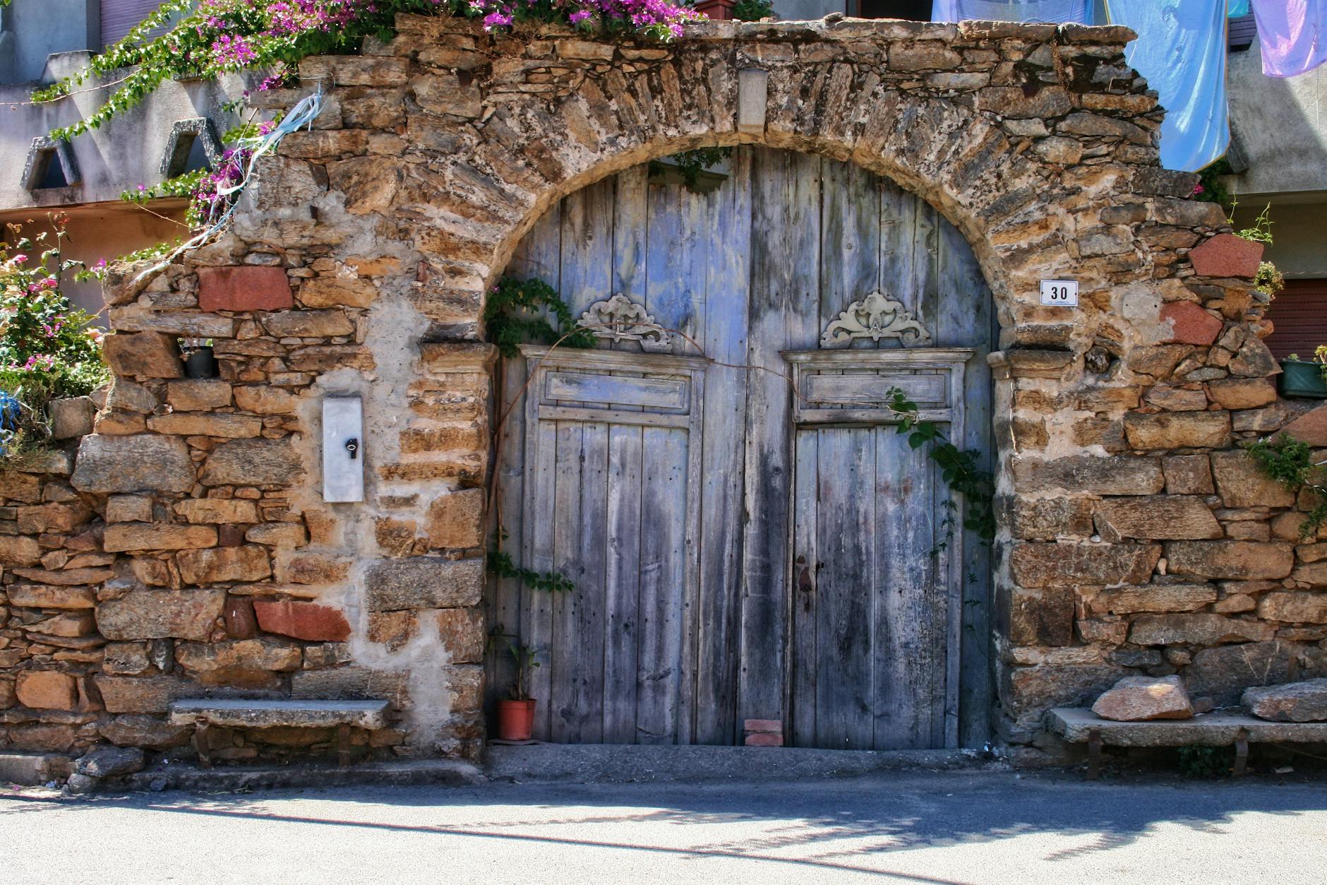 Historic stone archway with wooden doors in sunny Sardinia, Italy.
