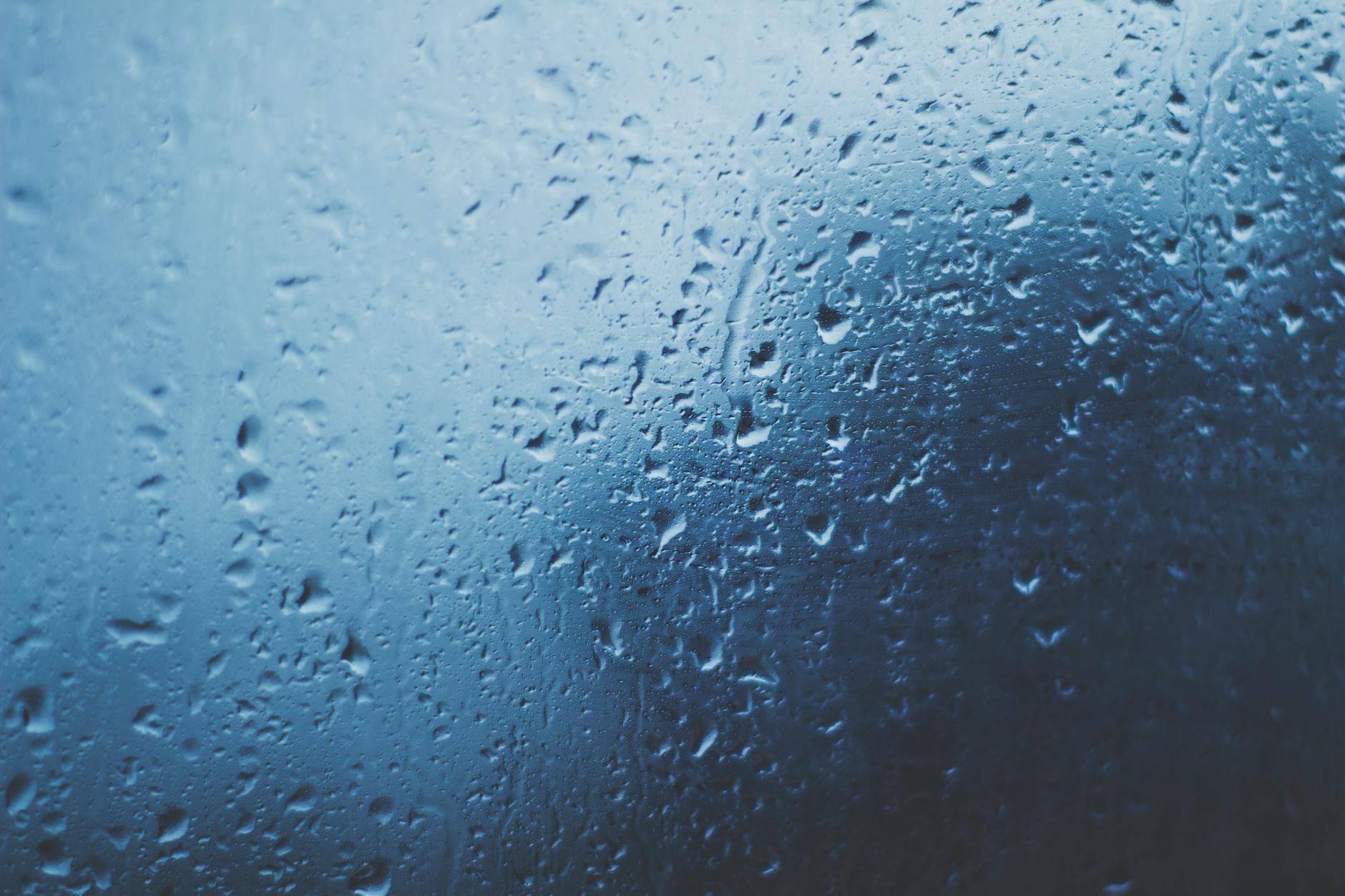 Detailed view of water droplets on a glass window with a blue background. Detailed view of water droplets on a glass window with a blue background.