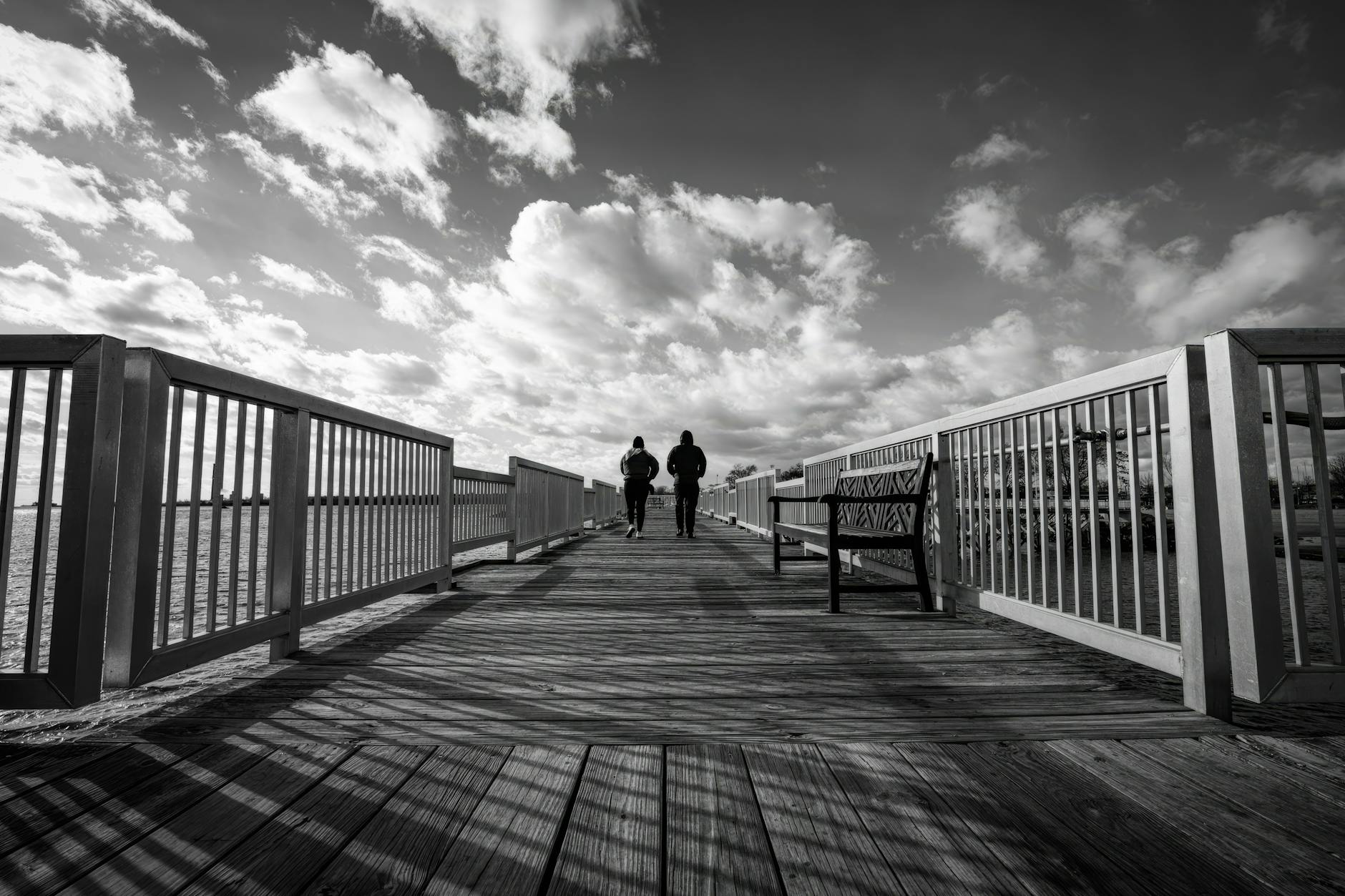Two people walking on a pier under a dramatic cloudy sky. Captures a moody, contemplative scene. Two people walking on a pier under a dramatic cloudy sky. Captures a moody, contemplative scene.