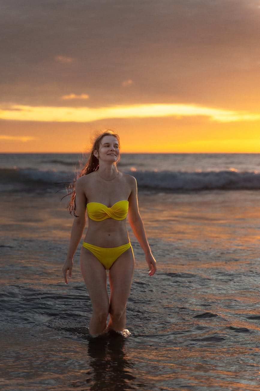 Woman in yellow bikini walks in ocean at Phuket, Thailand during sunset, embracing nature. Woman in yellow bikini walks in ocean at Phuket, Thailand during sunset, embracing nature.