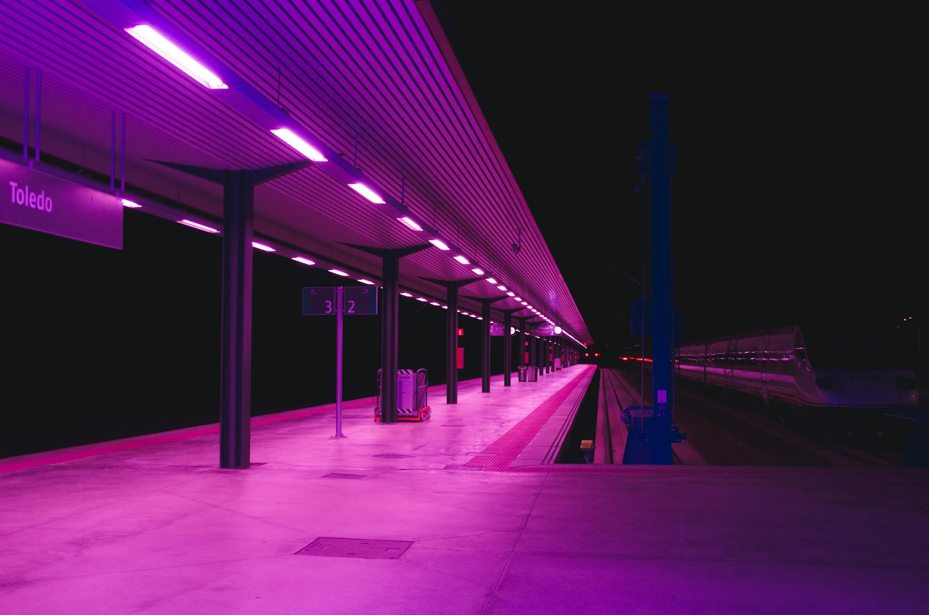 Explore the vibrant neon-lit train station platform in Toledo at night, showcasing urban architecture. Explore the vibrant neon-lit train station platform in Toledo at night, showcasing urban architecture.