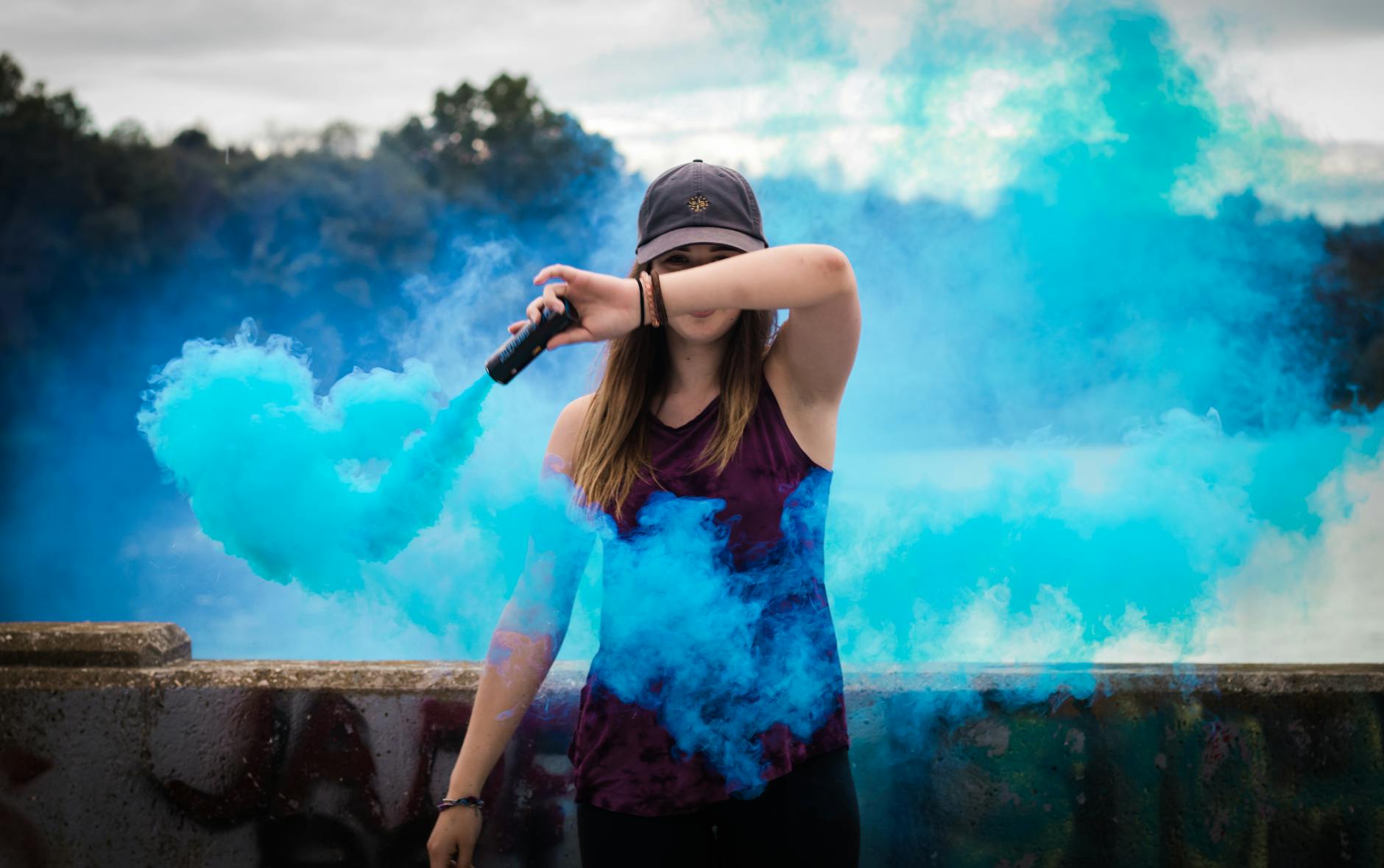 A stylish woman surrounded by bright blue smoke outdoors, creating a dynamic fashion statement. A stylish woman surrounded by bright blue smoke outdoors, creating a dynamic fashion statement.