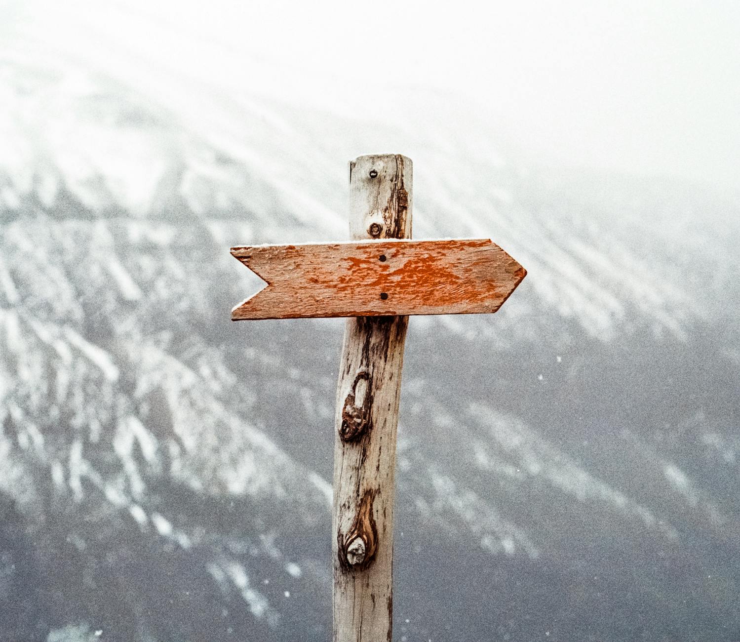 A wooden arrow signpost points the way amidst a snowy mountain landscape. A wooden arrow signpost points the way amidst a snowy mountain landscape.