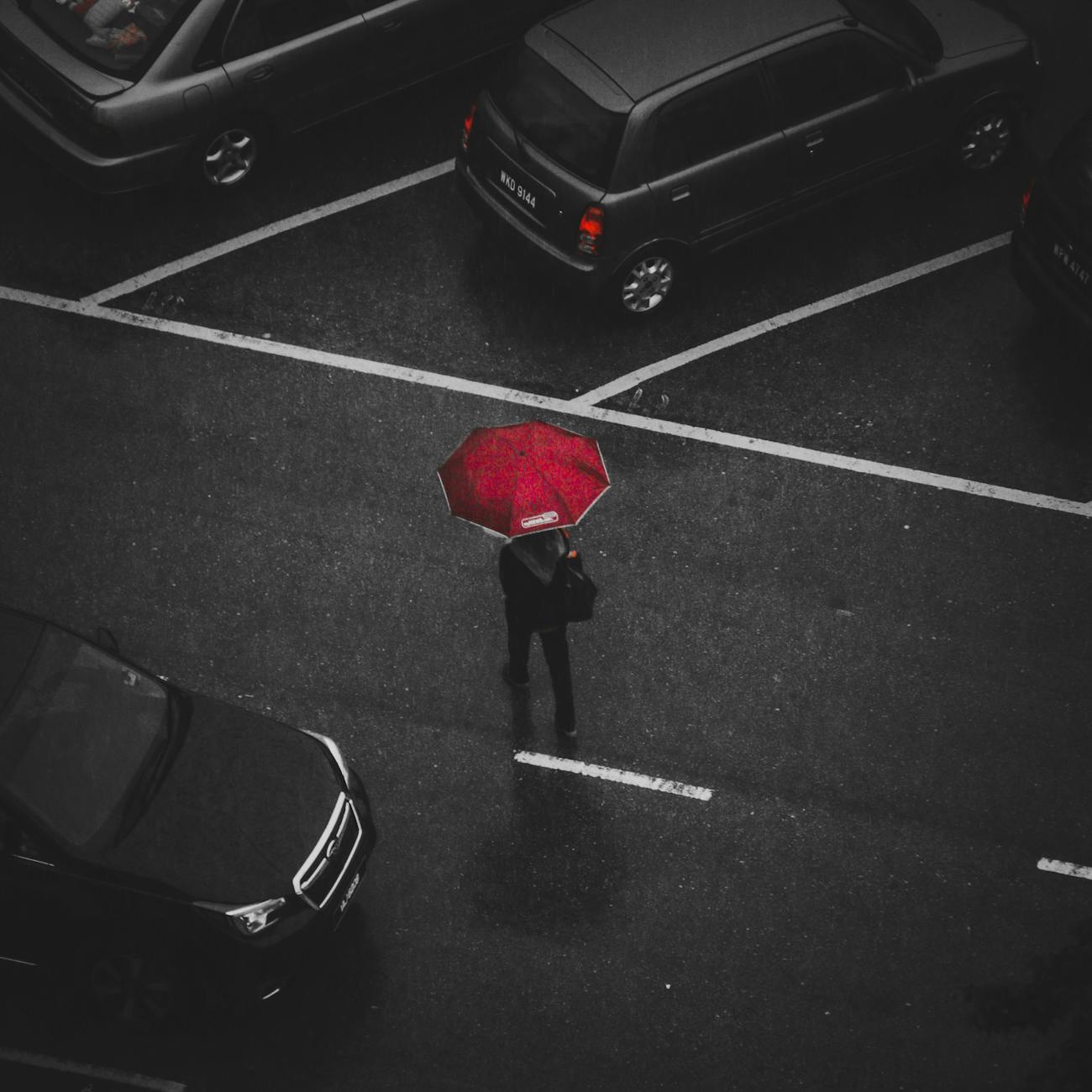 Top view of a person with a red umbrella walking in a rainy parking lot. Top view of a person with a red umbrella walking in a rainy parking lot.
