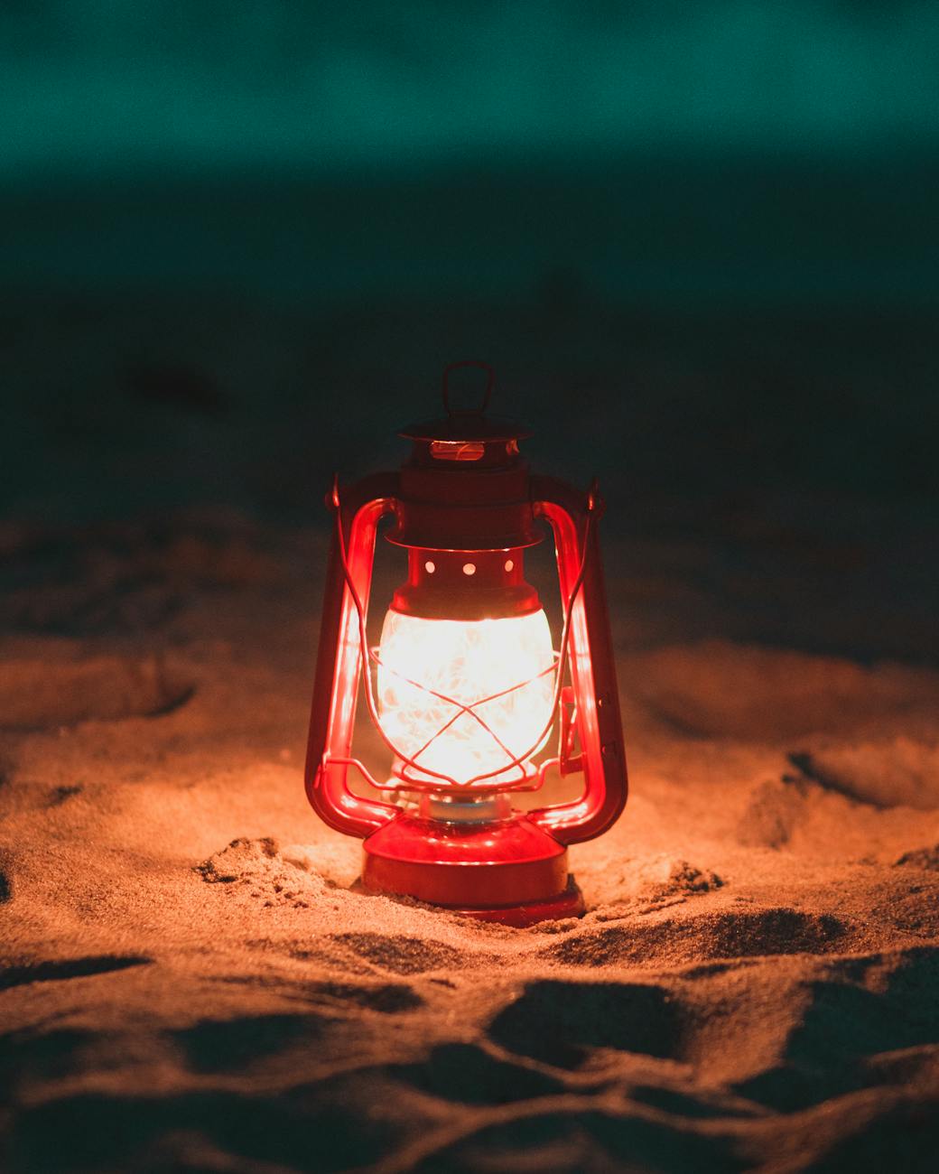 A glowing red lantern lights up the sandy beach during nighttime, creating a warm, cozy atmosphere.